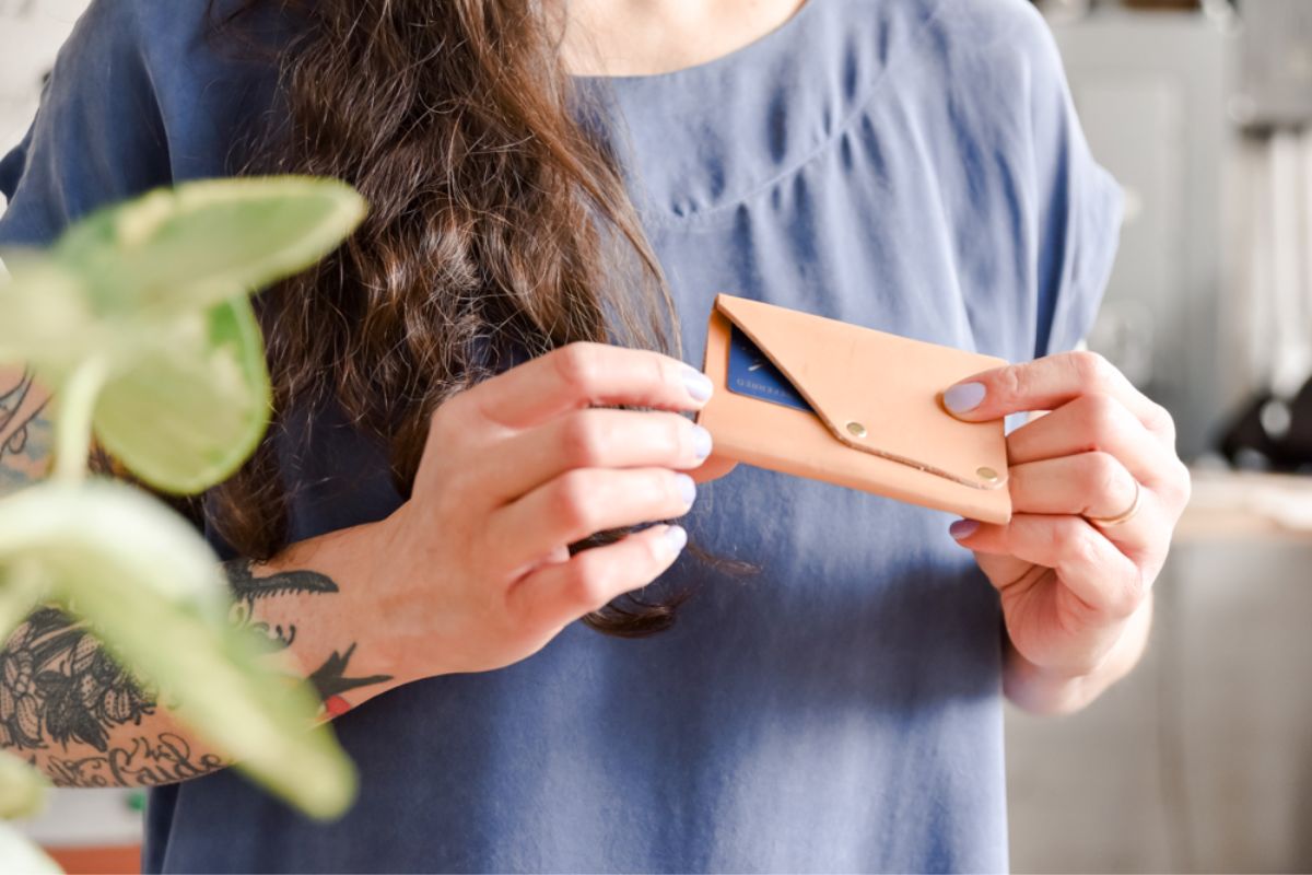 A woman holding an open tan leather card holder with a card tucked inside