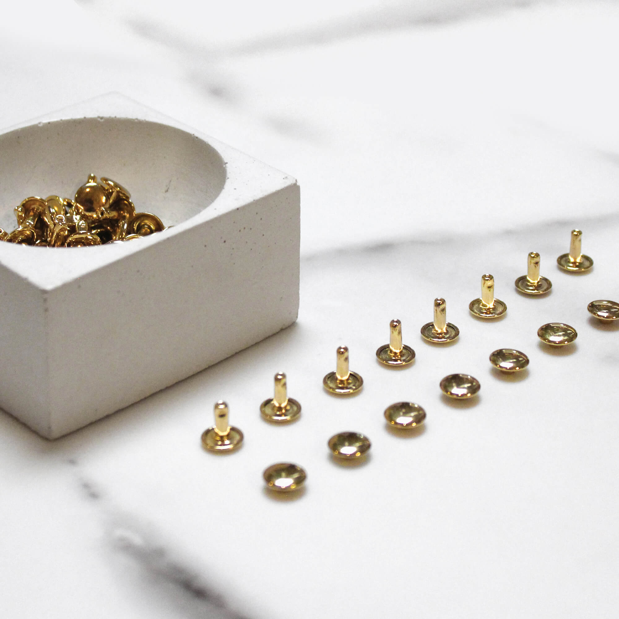 Brass double-cap rivets arranged on white marble - Klum House
