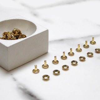 Brass double-cap rivets arranged on white marble - Klum House